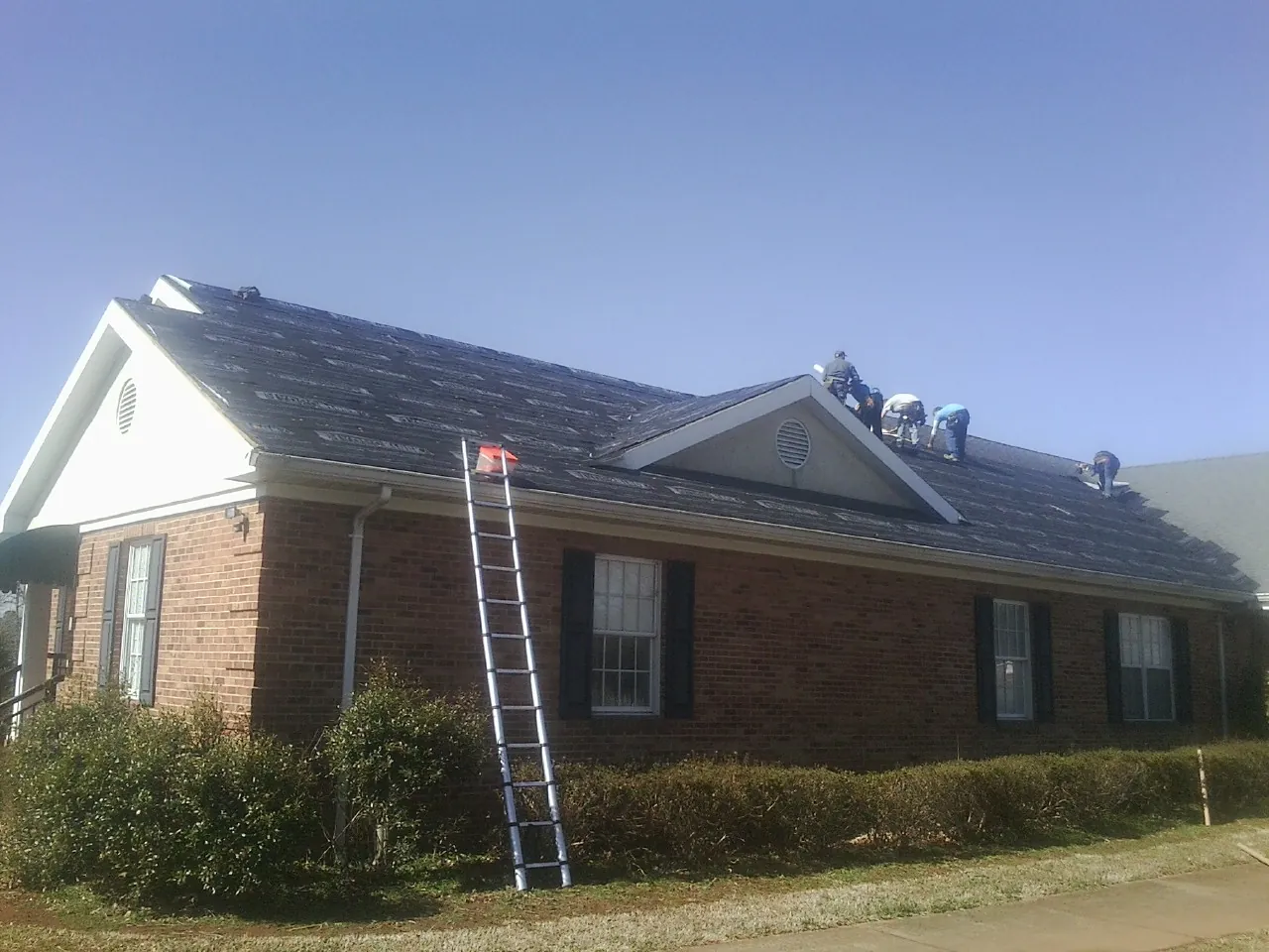 Crew tearing shingles off a brick ranch roof with a ladder set — Metal Roof Repair work by our crew in West Wareham