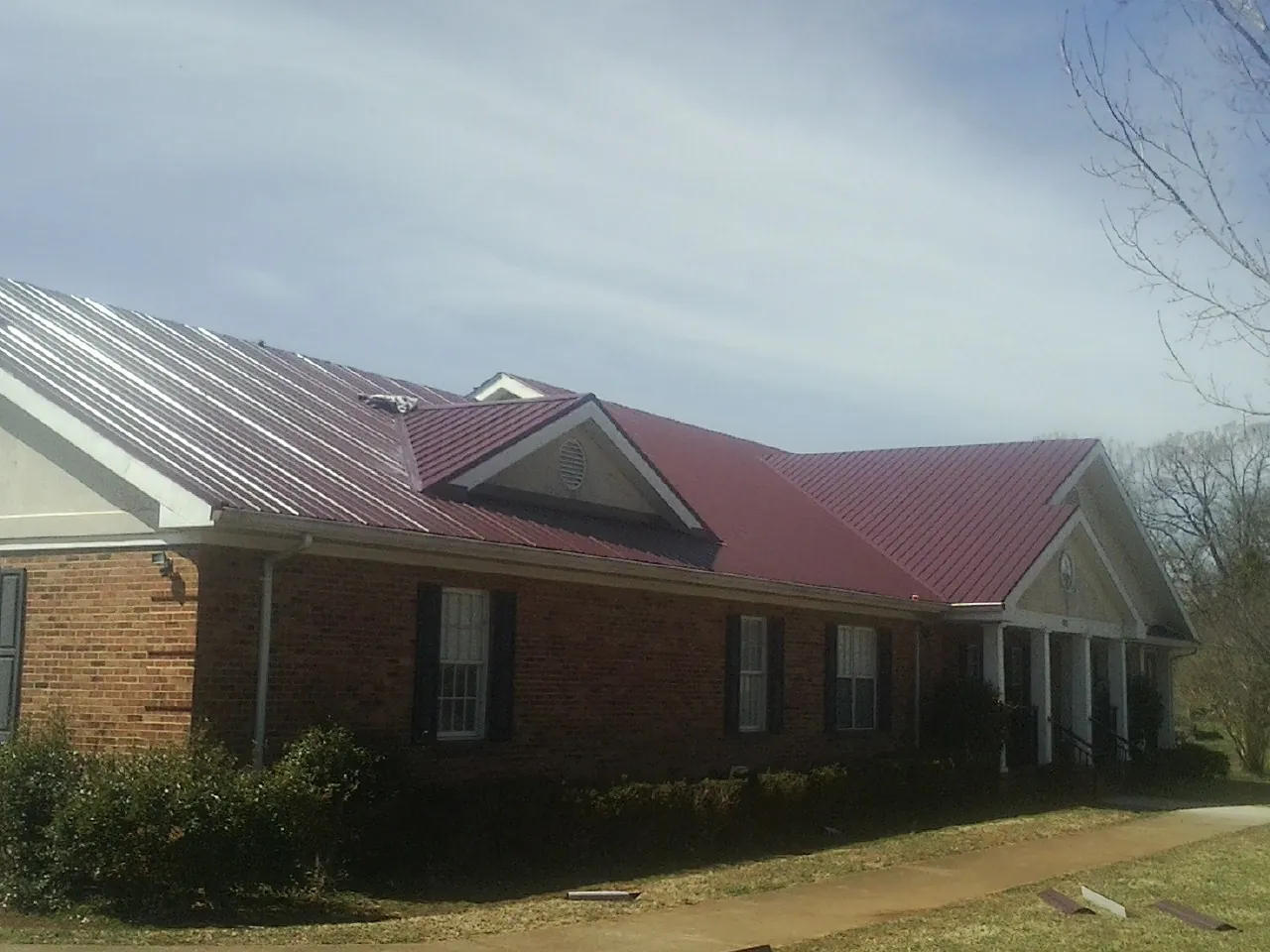 Red metal roof with gabled entries on a long brick building, from a Hail Damage Roof Repair job in West Wareham