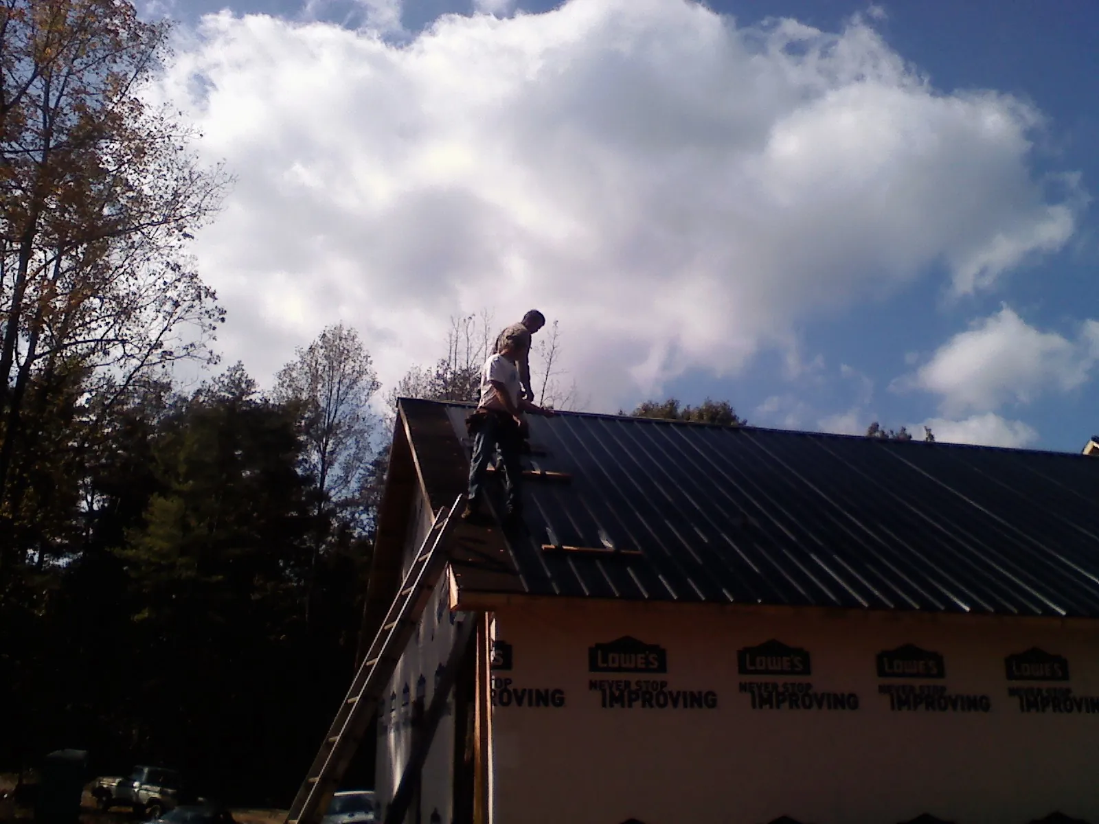 Roofer fastening dark metal panels high against a cloudy sky, from a Roof Inspection job in West Wareham
