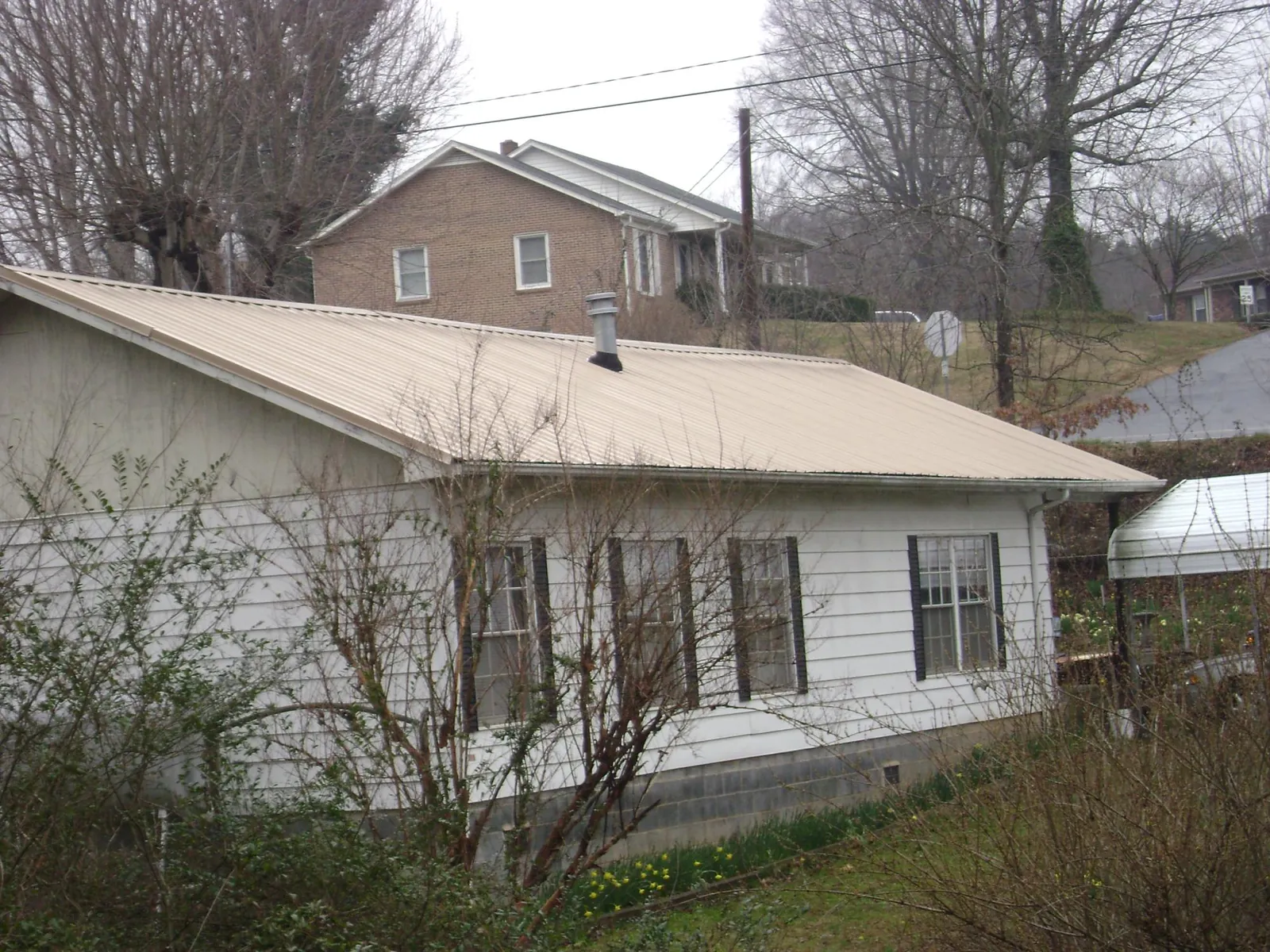 Tan metal roof on a white sided house set into a hillside — Commercial Roofing by Roofing Brothers in West Wareham